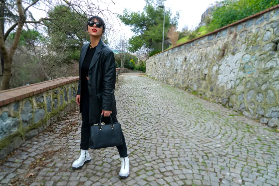 Selbstbewusste Frau in schwarzem Outfit trägt eine elegante schwarze Handtasche auf einem gepflasterten Weg – Sinnbild für Freiheit, Individualität und persönlichen Stil.