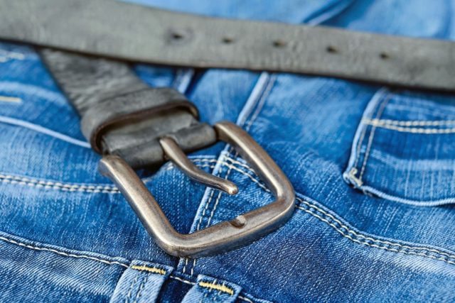 Ein Gürtel liegt auf der Jeanshose | Rabatt-Coupon