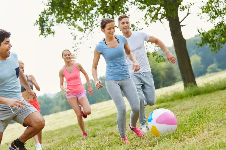 Rabattcoupons Gruppe junger Menschen spielt gemeinsam mit einem Ball auf einer Wiese im Park