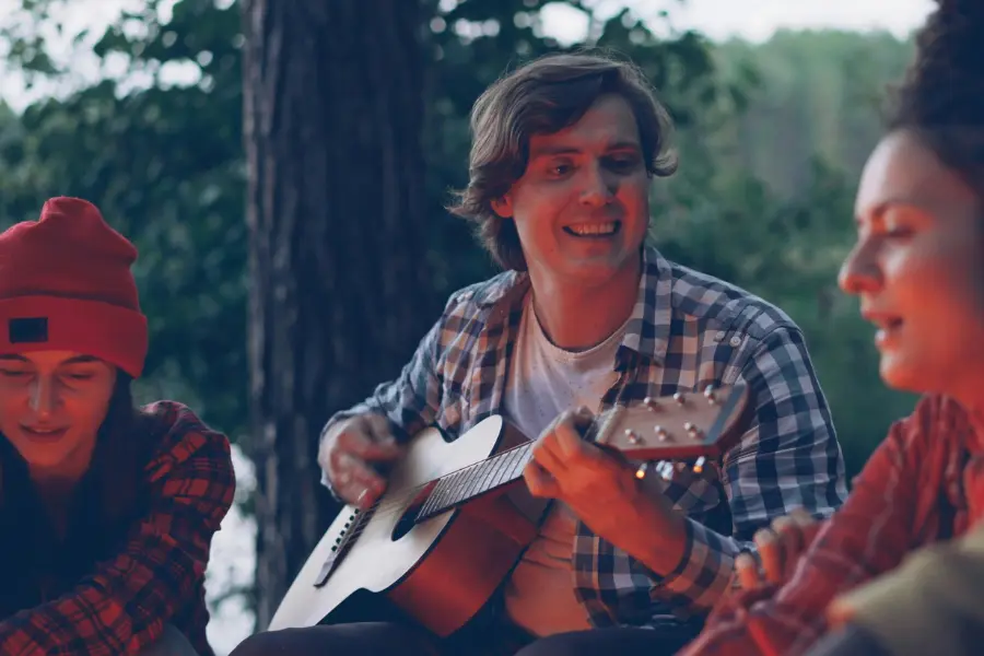 Freunde sitzen am Lagerfeuer und spielen Gitarre in der Natur