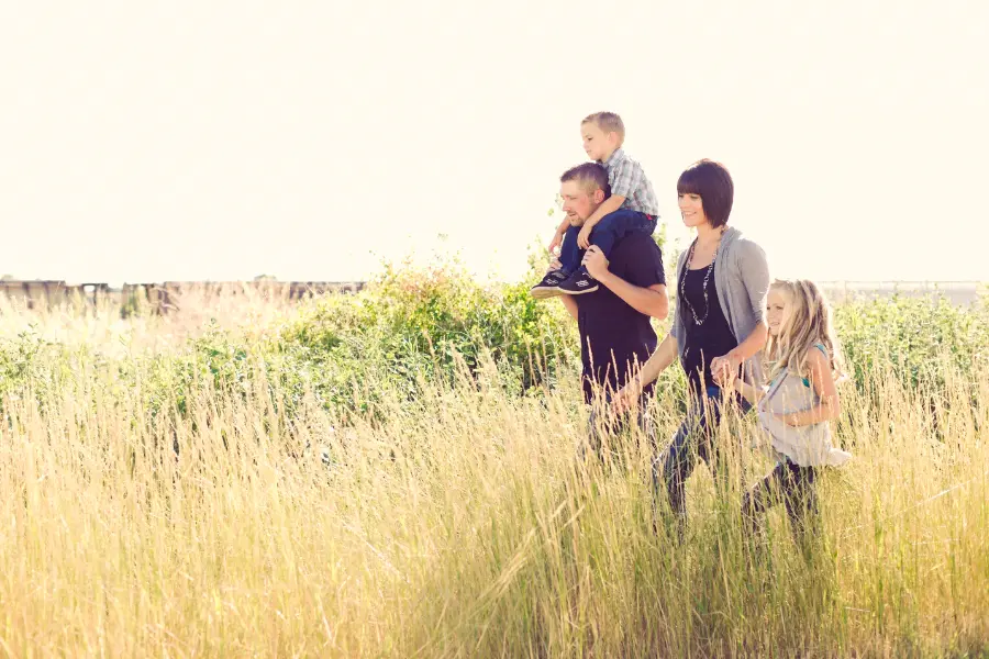 Rabatt Coupons Fröhliche Familie mit heller, langer Kleidung spaziert durch hohes Gras in der Natur – ein Beispiel für effektiven Mückenschutz durch geeignete Kleidung im Alltag.
