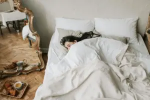 Frau schläft gemütlich unter heller, weicher Bettwäsche in einem herbstlich eingerichteten Schlafzimmer.