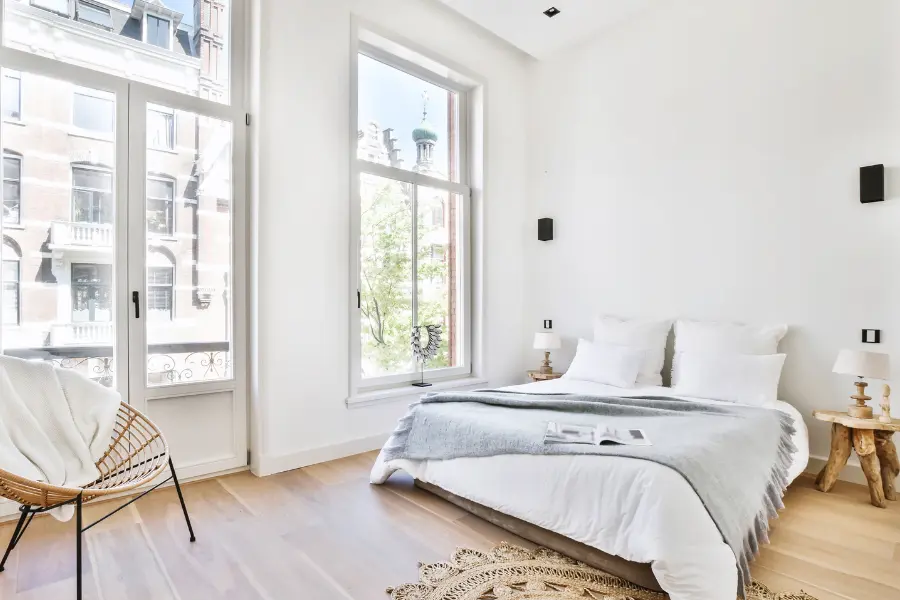 Rabatte Coupons Helles Schlafzimmer mit großen Fenstern, weißen Wänden, Naturholzboden, weißem Bett und minimalistischem Dekor.