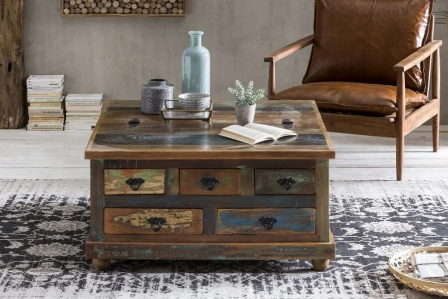 Rabatte Coupons Altholz Truhe im Vintage-Stil als Couchtisch in einem Wohnzimmer mit Lederstuhl, Teppich und dekorativen Accessoires.