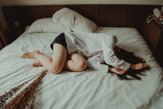Eine Frau liegt auf dem Bett und hält sich die Arme über dem Kopf | Rabatte Coupons