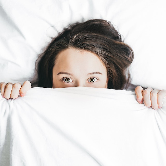 Eine Frau versteckt ihr Gesicht unter der Bettdecke | rabatte coupon