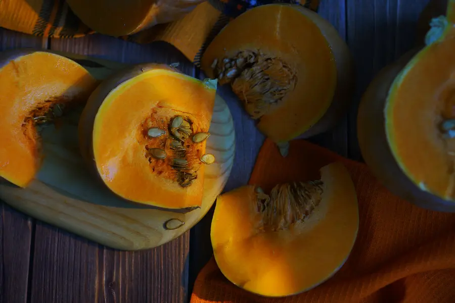 Aufgeschnittene orangefarbene Kürbisse mit sichtbaren Kernen liegen auf einem dunklen Holztisch – ein stimmungsvolles Bild für den Beginn der Kürbissaison im Herbst.