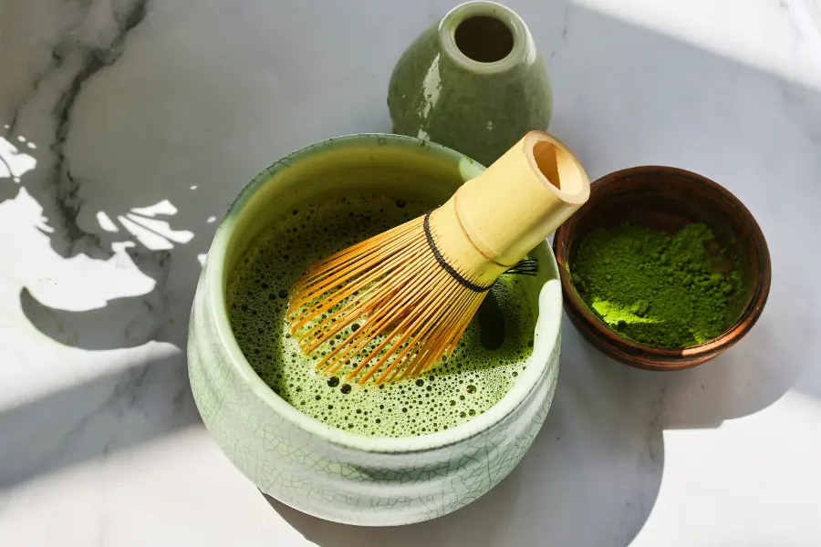 Frisch zubereiteter Matcha-Tee in einer grünen Schale mit Bambusbesen und feinem Matcha-Pulver.