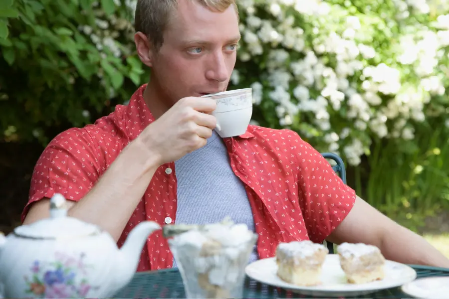 Mann trinkt im Sommer draußen im Garten eine Tasse Tee zu Gebäck und genießt eine entspannte Teepause.