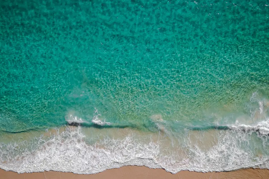 Aerial view of turquoise ocean waves washing onto a sandy beach shoreline.