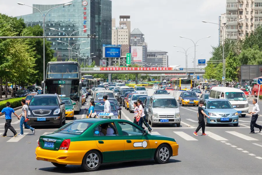 Busy city intersection in China with taxis, buses, cars, and pedestrians crossing in daytime traffic.
