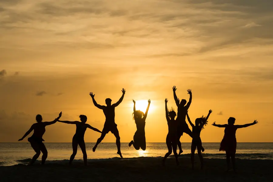 Silhouetted group of friends jumping and celebrating on a beach at sunset.