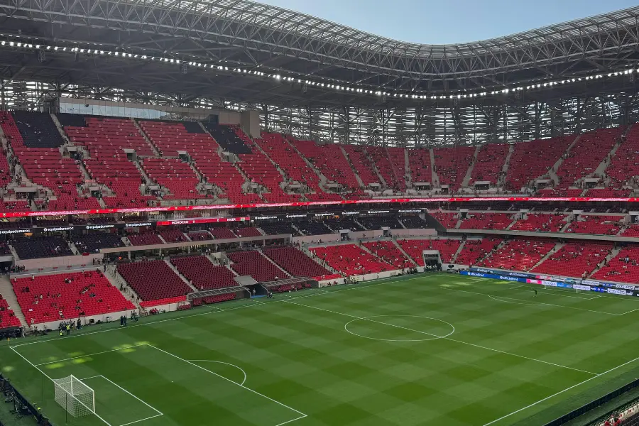 Large modern soccer stadium with red seating, a green pitch, and a partially covered roof.