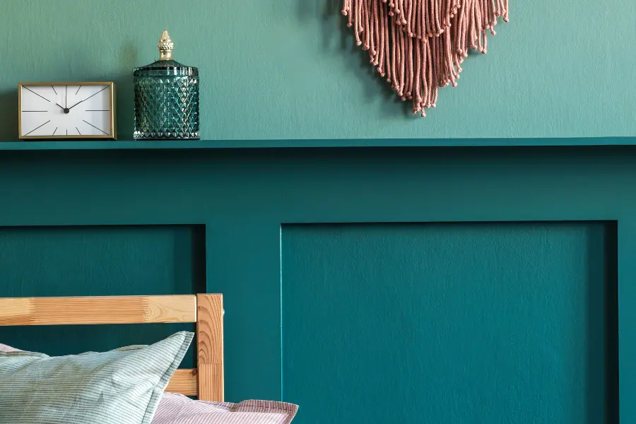 Welche sind die neuen Wohntrends für 2021? Das ratet euch der Home-Soul Gutschein. Teal bedroom wall with wooden bed frame, pillows, shelf decor, a small clock, glass jar, and woven wall hanging.