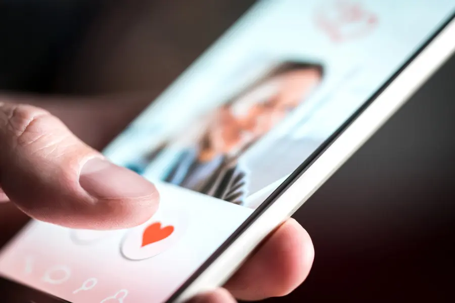 Ohne den Amorelie Gutschein ist die Partnersuche im Internet nutzlos. Close-up of a person tapping a heart icon on a smartphone dating app profile.