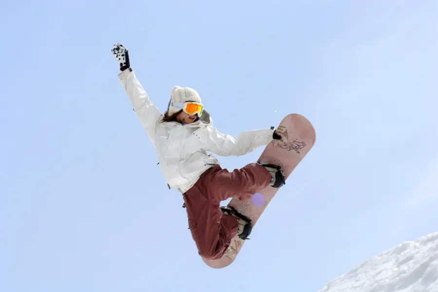 Sichert euch jetzt bei der The North Face Aktion den kostenlosen Versand bei eurer Bestellung ohne Mindestbestellwert. Snowboarderin springt mit Snowboard vor blauem Himmel über eine verschneite Piste.