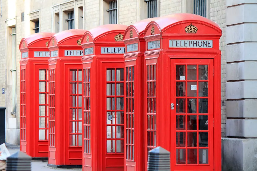 Die Geschichte des Telefons 🐼 von der Erfindung bis heute 5 Row of iconic red British telephone booths on a city sidewalk in front of a stone building.