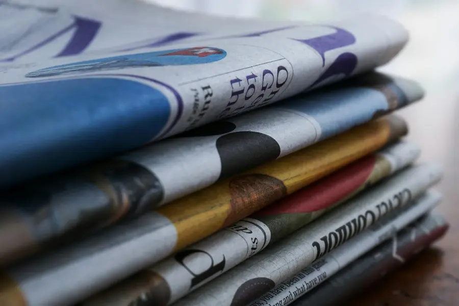 Smartphone & Co. übernehmen 🐼 Hat die Printzeitung ausgedient? 3 Stapel gefalteter Zeitungen in Nahaufnahme mit sichtbaren Druckseiten und unscharfem Hintergrund.