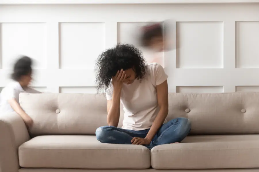 Seifenblasen sind bunt und machen Spaß. Filterblasen sind eintönig. Gestresste Frau sitzt auf einem Sofa und hält sich die Stirn, während verschwommene Personen im Hintergrund Bewegung und Unruhe andeuten.