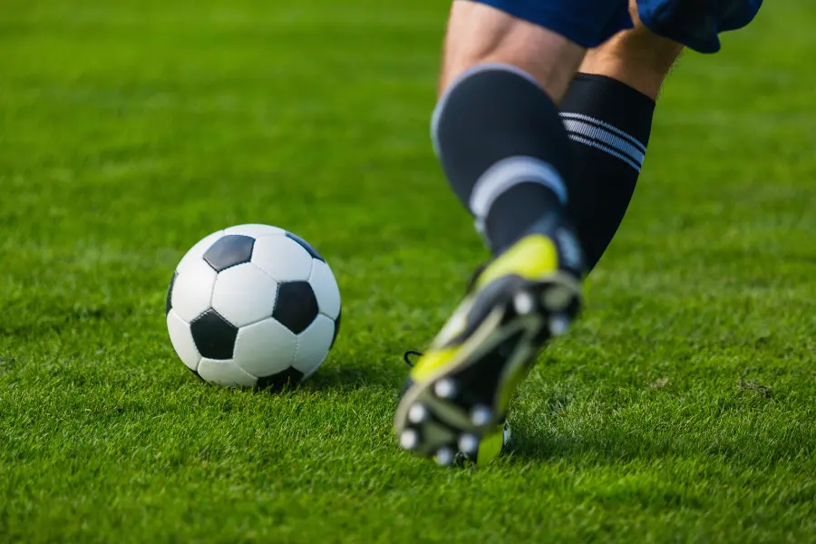 Fußballspieler läuft auf grünem Rasen zum Ball und setzt zum Schuss an.