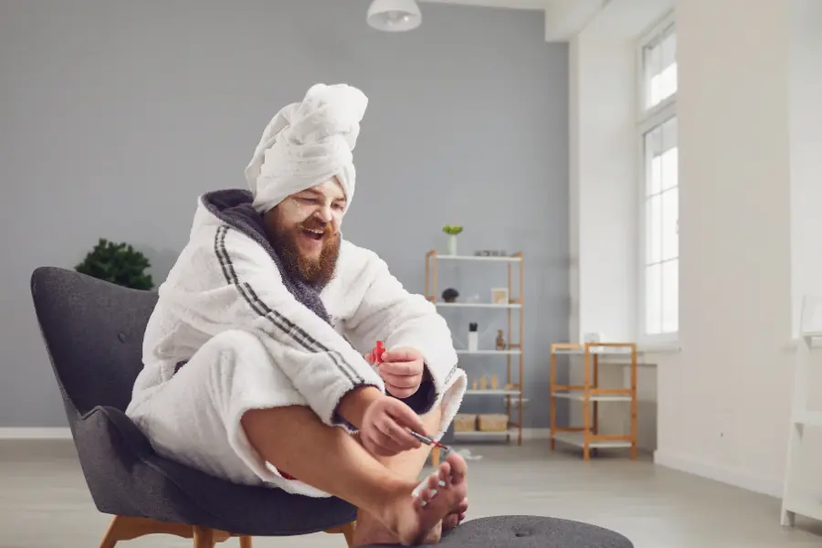 Füße pflegen - diese Tipps garantieren strahlende Sommerfüße | www.rabatt-coupon.com Mann in Bademantel und mit Handtuchturban sitzt entspannt auf einem Sessel und pflegt seine Fußnägel mit Nagellack.