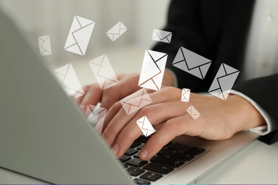 Hände tippen auf einem Laptop mit schwebenden Briefumschlägen als Symbol für E-Mail-Kommunikation.