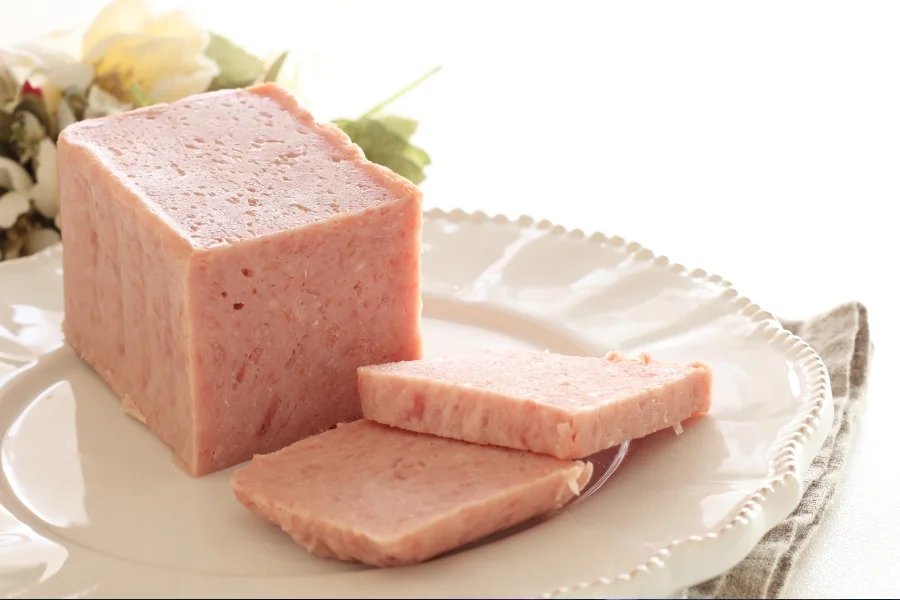 Rosa Fleischblock mit zwei aufgeschnittenen Scheiben auf einem weißen Teller.