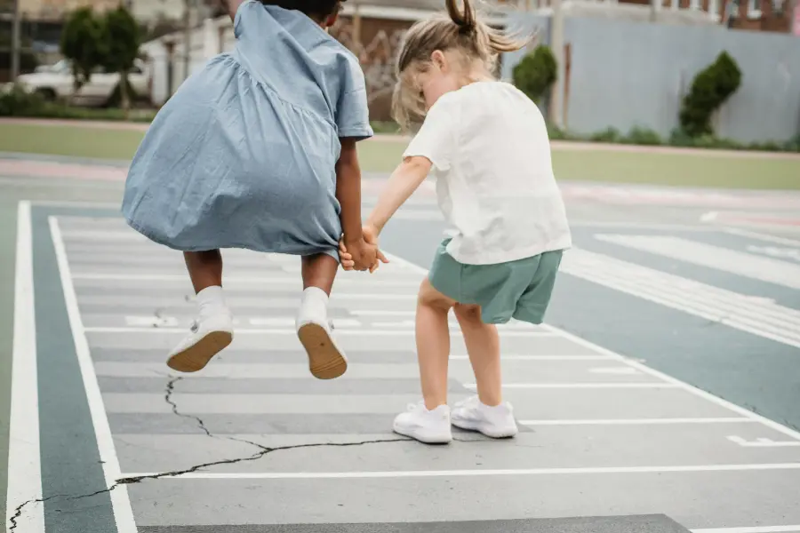 Selbstbewusste Kinder schätzen beide Leben. Mit dem o2 Gutschein könnt ihr sowohl im virtuellen als auch im echten Leben tolle Deals ergattern. Zwei Kinder springen auf einem Spielfeld im Freien, Hand in Hand, lachend und voller Bewegung – Momentaufnahme kindlicher Lebensfreude und echter Begegnung.