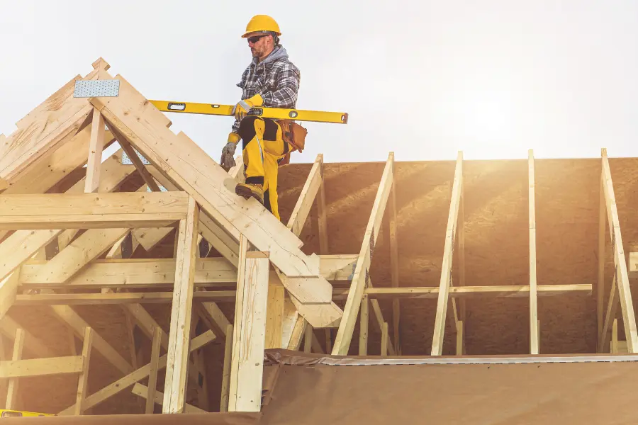 Möbelhaus Ostermann und Hausbauen passt perfekt. Ein Handwerker mit Schutzhelm und Wasserwaage arbeitet auf dem Dachstuhl eines im Bau befindlichen Hauses aus Holz.