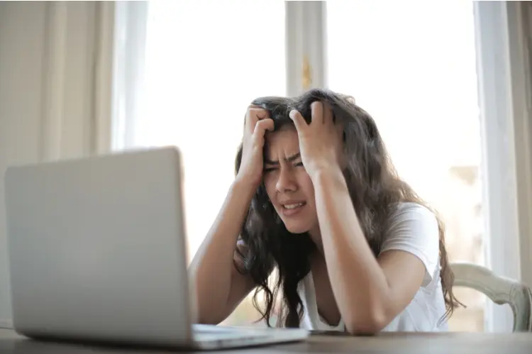 Gestresste Frau sitzt vor einem Laptop und hält sich verzweifelt den Kopf